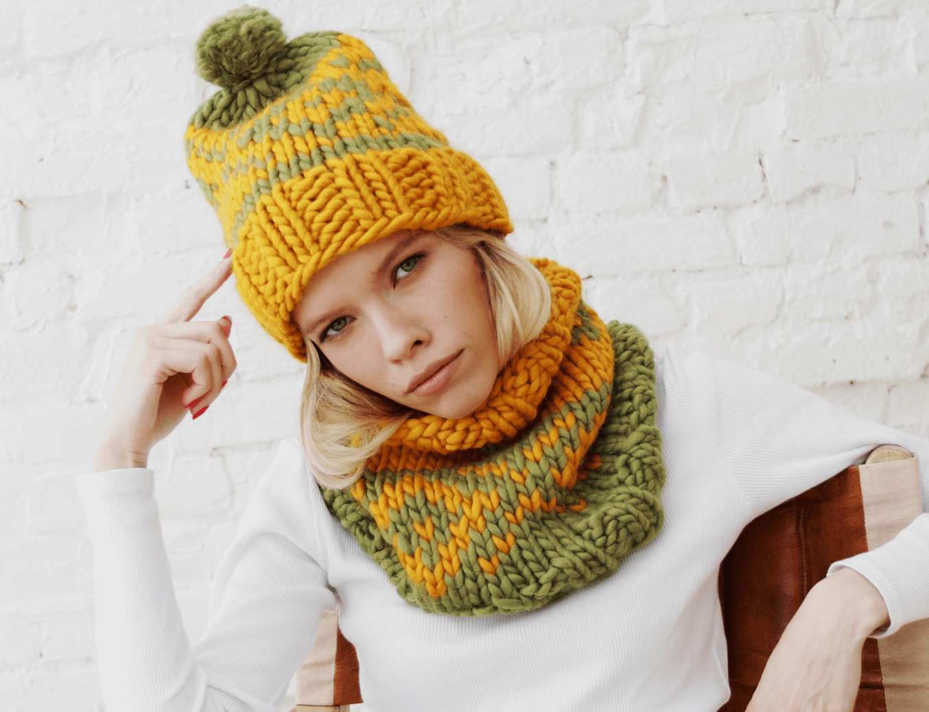 Person wearing a yellow and green knitted hat and scarf on a white background